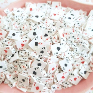 May include: A bowl filled with white plastic playing card confetti. The cards are decorated with red hearts, black spades, diamonds, and clubs. The cards are all aces.