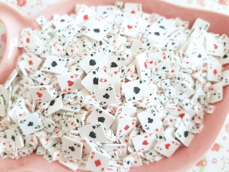 May include: A bowl filled with white plastic playing card confetti. The cards are decorated with red hearts, black spades, diamonds, and clubs. The cards are all aces.