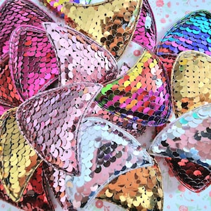 May include: A collection of colorful, iridescent, sequined, fishtail-shaped patches. The patches are made of various colors, including pink, gold, silver, and purple.