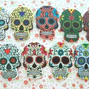 May include: Ten colorful sugar skull charms with intricate designs. Each charm features a different pattern of flowers, swirls, and hearts. The charms are made of wood and have a glossy finish.
