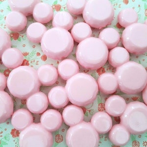 Op de afbeelding: Een verzameling roze, gefacetteerde, Mickey Mouse-kopvormige charmes van plastic. De charmes zijn in een willekeurig patroon gerangschikt.