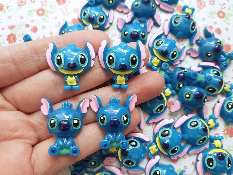 May include: A collection of blue and yellow Stitch character charms. The charms are made of resin and have a glossy finish.