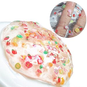 May include: Clear slime with a variety of colorful fruit and flower shaped charms. The slime is spread out on a white surface.