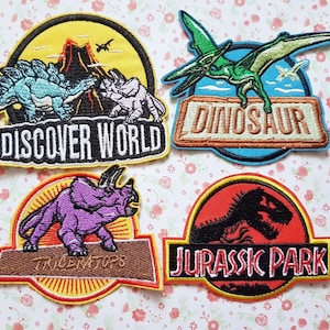May include: Four embroidered iron-on patches featuring dinosaurs. The patches are yellow, blue, red, and purple with black outlines. The patches feature the text "Discover World", "Dinosaur", "Triceratops", and "Jurassic Park".
