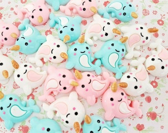 May include: A collection of colourful narwhal charms in pink, blue and white. The charms are made of resin and have a glossy finish. They are perfect for adding a touch of whimsy to your crafts.