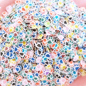 May include: A large pile of colorful paw print shaped sprinkles. The sprinkles are white with different colored accents, including blue, green, pink, orange, yellow, and brown.