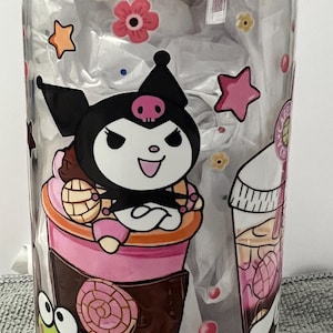 Pu&ograve; includere: Un barattolo di vetro trasparente con un coperchio di legno presenta un design di cartoni animati colorato. Il design include una tazza rosa e marrone con un personaggio nero e bianco con un teschio sulla testa. Il personaggio &egrave; circondato da stelle rosa e bianche, fiori rosa e caramelle rosa e bianche.
