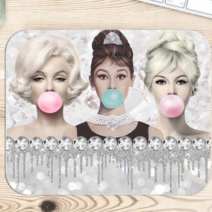May include: Rectangular mousepad featuring three iconic women blowing bubblegum bubbles. The women are Marilyn Monroe, Audrey Hepburn, and another blonde woman. The design includes a silver glitter border with crystal accents and a sparkling background.