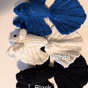 May include: Crocheted betta fish in royal blue, white, and black. Each fish has a detailed tail and fins, with a small black eye. The word "Royal", "White", and "Black" are written above each fish.