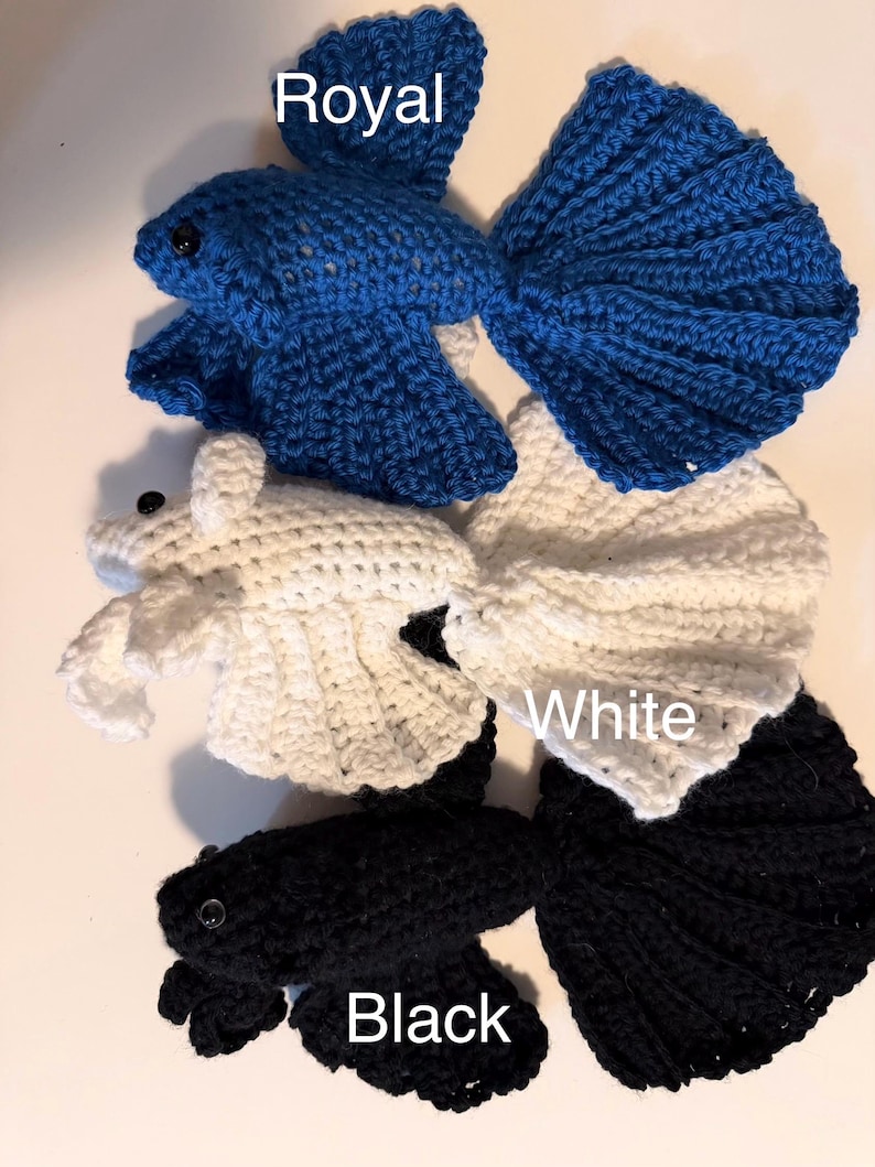 May include: Crocheted betta fish in royal blue, white, and black. Each fish has a detailed tail and fins, with a small black eye. The word "Royal", "White", and "Black" are written above each fish.