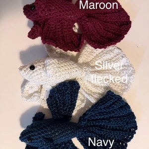 May include: Three crocheted betta fish in maroon, silver flecked, and navy blue. Each fish has a detailed tail and fins, with a small black eye. The fish are handmade and appear to be soft and plush.