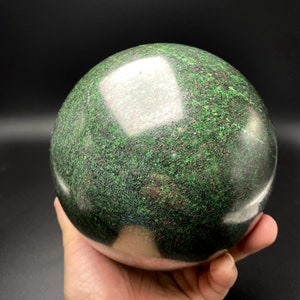 May include: A polished green sphere with red and silver flecks. The sphere is made of natural stone and has a smooth, shiny surface.