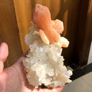 以下が含まれることがあります： 透明な水晶のクラスターの上に、大きなオレンジ色のカルサイトの結晶が乗っています。結晶は自然で有機的な形に配置されています。