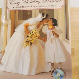May include: A wedding planner book titled "Easy Wedding Planner" with a photo of a bride kissing a young girl. The book cover features a bride in a white gown holding a bouquet, and a young girl in a white dress. A CD-ROM is included.