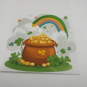 May include: A brown pot filled with gold coins sits in front of a rainbow and clouds. Green shamrocks are scattered around the pot and in the clouds.