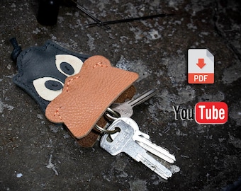 May include: A leather key chain shaped like a cartoon duck with a black and white face and an orange beak. The keychain has a metal ring for attaching keys. The image also includes a PDF download icon and a YouTube logo.