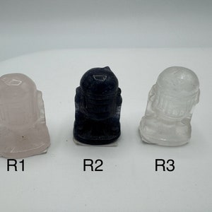 May include: Three small figurines of a robot character, one is pink, one is black, and one is clear.