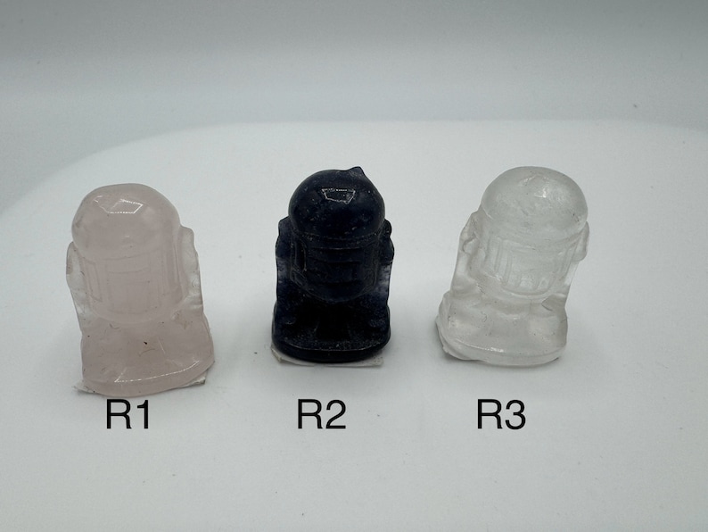 May include: Three small figurines of a robot character, one is pink, one is black, and one is clear.