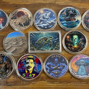 May include: A collection of eleven circular coins and one rectangular bar, each featuring distinct colorful illustrations including a mermaid, wolf, yeti, pirate ship, eye, desert, sea turtle, alien abduction, Zeus, Charles Ponzi, and a genie.