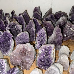 May include: A collection of amethyst crystal clusters in various sizes and shapes. The crystals are a deep purple colour and have a natural, rough texture.