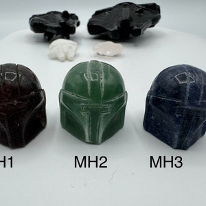 May include: Three Mandalorian helmet-shaped resin figurines. The helmets are in different colors: dark brown, green, and blue. The helmets are labeled MH1, MH2, and MH3.