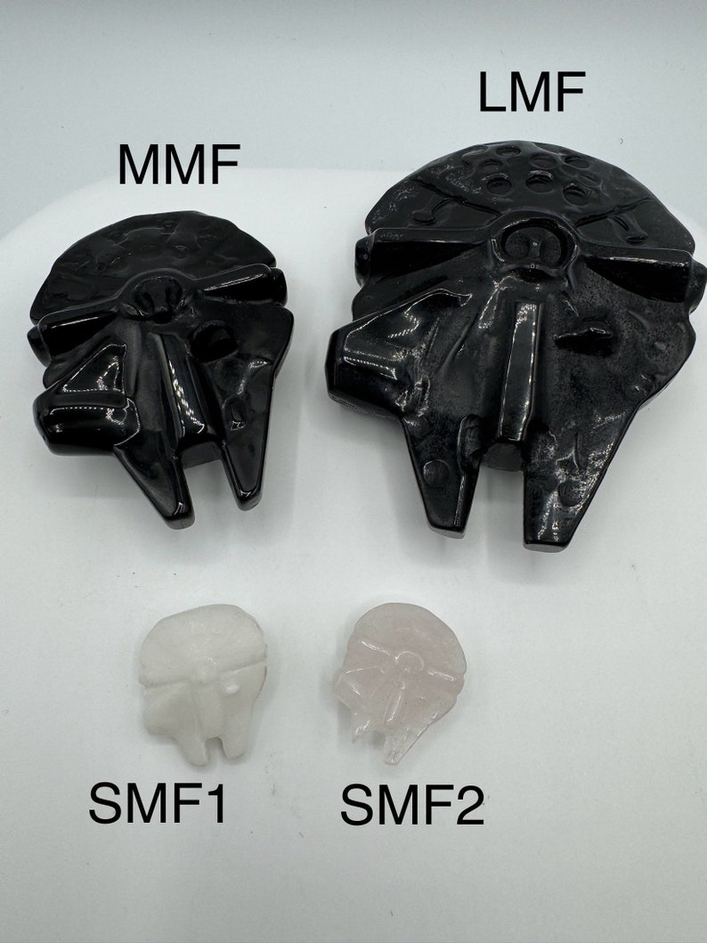 May include: Three black and white resin Star Wars Millennium Falcon models. The largest model is labeled "LMF", the medium model is labeled "MMF", and the smallest model is labeled "SMF1". A smaller, pink resin model is labeled "SMF2".