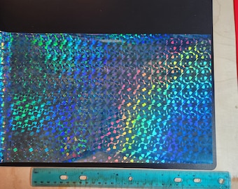 以下が含まれることがあります： 幾何学模様の虹色のホログラフィックビニールシート。ビニールは青、緑、紫で、虹色の効果があります。