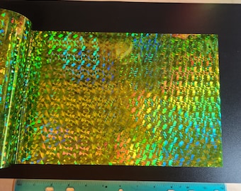 May include: A sheet of iridescent green holographic vinyl with a geometric pattern. The vinyl has a shiny, reflective surface.