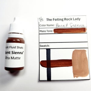 May include: A small bottle of Burnt Sienna acrylic fluid shots in an ultra matte finish. The bottle is labeled with the product name and the brand "The Foiling Rock Lady". A color swatch shows the color Burnt Sienna.