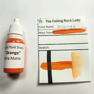 May include: A small bottle of orange acrylic paint labeled "Acrylic Fluid Shots "Orange" Ultra Matte". A swatch card shows the color of the paint, labeled "The Foiling Rock Lady" and "Orange".