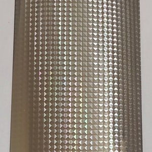 Puede incluir: Primer plano de una lámina de vinilo holográfico iridiscente con un patrón repetitivo de pequeños triángulos. El vinilo tiene un brillo sutil y un brillo metálico.