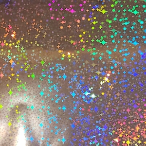 May include: A sheet of iridescent holographic paper with a repeating pattern of stars in various colors, including blue, green, pink, and yellow.