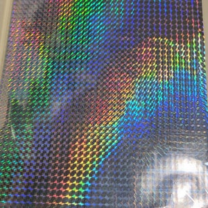 May include: A sheet of iridescent holographic film with a repeating pattern of small, diamond-shaped squares. The film has a rainbow effect with shades of blue, green, red, and yellow.