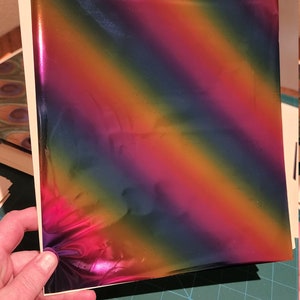 May include: A sheet of iridescent rainbow holographic vinyl with a diagonal pattern. The vinyl is on a green cutting mat.