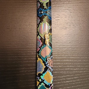 Può includere: Primo piano di un tessuto nero e iridescente con motivo a pelle di serpente con accenti blu, verdi, gialli e rosa.