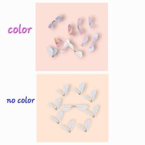 May include: Two sets of decorative wings. The top set features wings in various colors, including pink, purple, and yellow. The bottom set displays white wings. Both sets are arranged on a light pink and beige background.