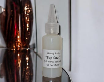 May include: A clear glass bottle with a white cap and label. The label reads "Glossy Shots "Top Coat" Roll to mix contents Do not shake".