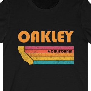 May include: Black t-shirt with a vintage-style graphic of the state of California with the text "OAKLEY" and "CALIFORNIA" in orange.