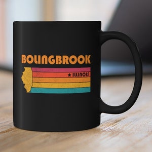 Pode incluir: Caneca de café de cerâmica preta com um design retro que apresenta o texto "Bolingbrook, Illinois" e um contorno estilizado do estado de Illinois com um padrão de listras arco-íris.