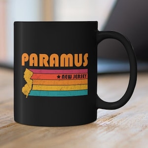 以下が含まれることがあります： オレンジ色の文字で「PARAMUS」と書かれた、レトロなデザインの黒いコーヒーカップ。虹色のレインボーカラーでスタイリッシュに描かれたニュージャージー州の輪郭が描かれている。州の輪郭の下には白い文字で「NEW JERSEY」と書かれている。