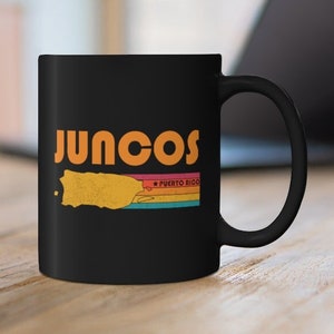Può includere: Tazza da caffè nera con un contorno bianco di Porto Rico e il testo "Juncos, Puerto Rico" in arancione.