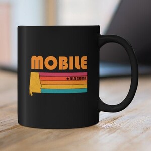 May include: Black ceramic coffee mug with a retro-style graphic of the state of Alabama with the word "MOBILE" and the text "*ALABAMA*" printed in white.
