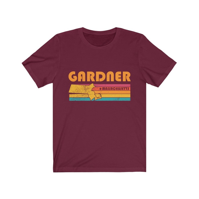 May include: A maroon t-shirt with a vintage-style graphic of the state of Massachusetts with the word "GARDNER" and "MASSACHUSETTS" in orange text.