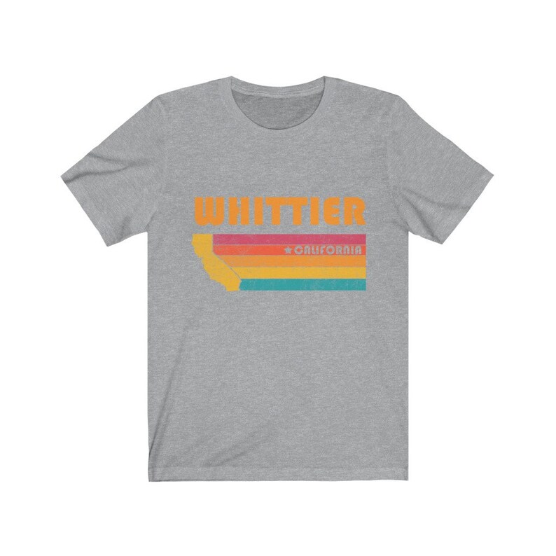 May include: A heather grey t-shirt with a retro-style graphic of the state of California with the text "WHITTIER" and "CALIFORNIA" in orange.
