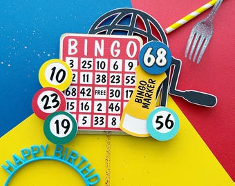 May include: A birthday party decoration set with a red, white, and blue bingo card, a globe, a paint roller, and a blue headband that says "Happy Birthday". There are also several colorful bingo chips with numbers on them.