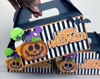May include: Three black and white striped Halloween treat boxes with orange and black pumpkin faces, candy corn, and bats. The boxes have a handle and say "Happy Halloween".