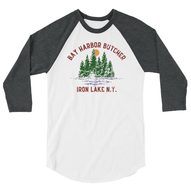 May include: A white and grey baseball tee shirt with a distressed graphic design of a forest scene with a red sun and the text "Bay Harbor Butcher Iron Lake N.Y."