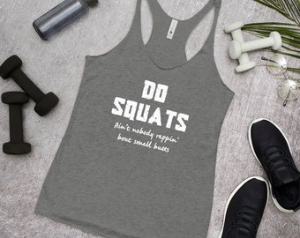 Puede incluir: Camiseta sin mangas gris con el texto "DO SQUATS" en letras blancas. Debajo, la frase "Ain't nobody rappin' bout small butts". La camiseta está sobre una superficie gris con equipo de entrenamiento.