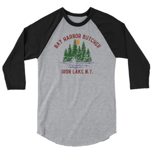 May include: A black and grey baseball tee shirt with a vintage design. The text on the shirt reads "Bay Harbor Butcher Iron Lake N.Y.".