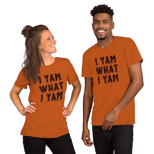 Op de afbeelding: Twee mensen dragen oranje T-shirts met de tekst "I yam what I yam" in zwart.